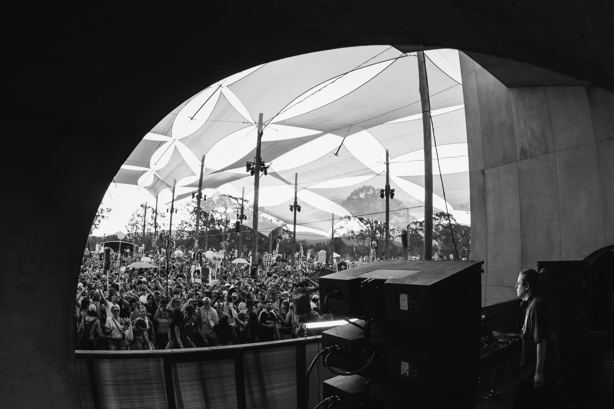 Festival crowd seen from the DJ booth through Pitch One's concrete arch, under a canopy of white shade sails