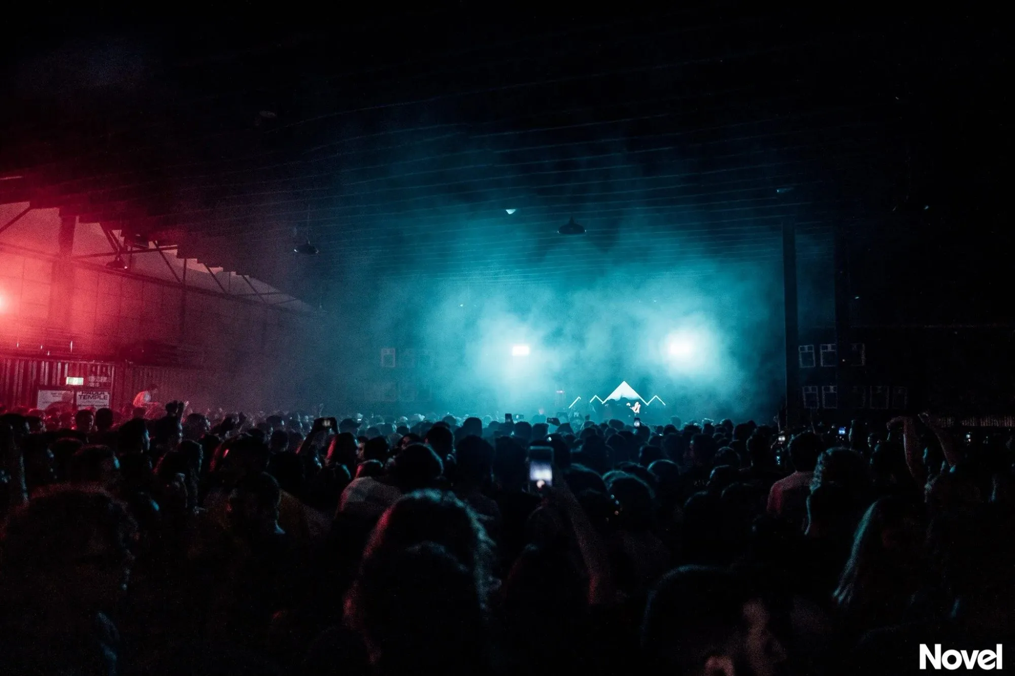 Glowing white peaked set piece cutting through teal haze above the crowd inside a dark warehouse